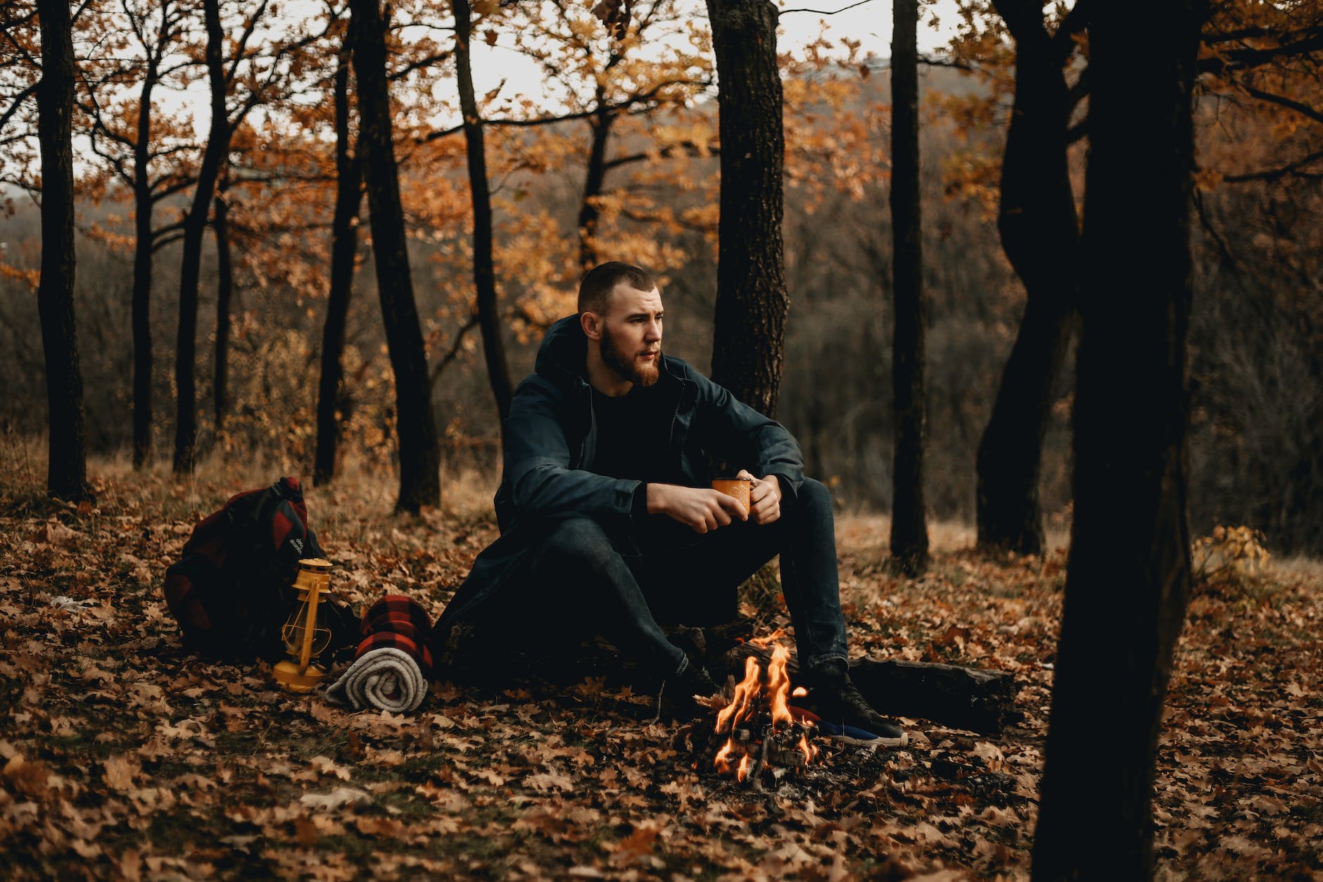 an adventurer holding a cup and sitting by the campfire